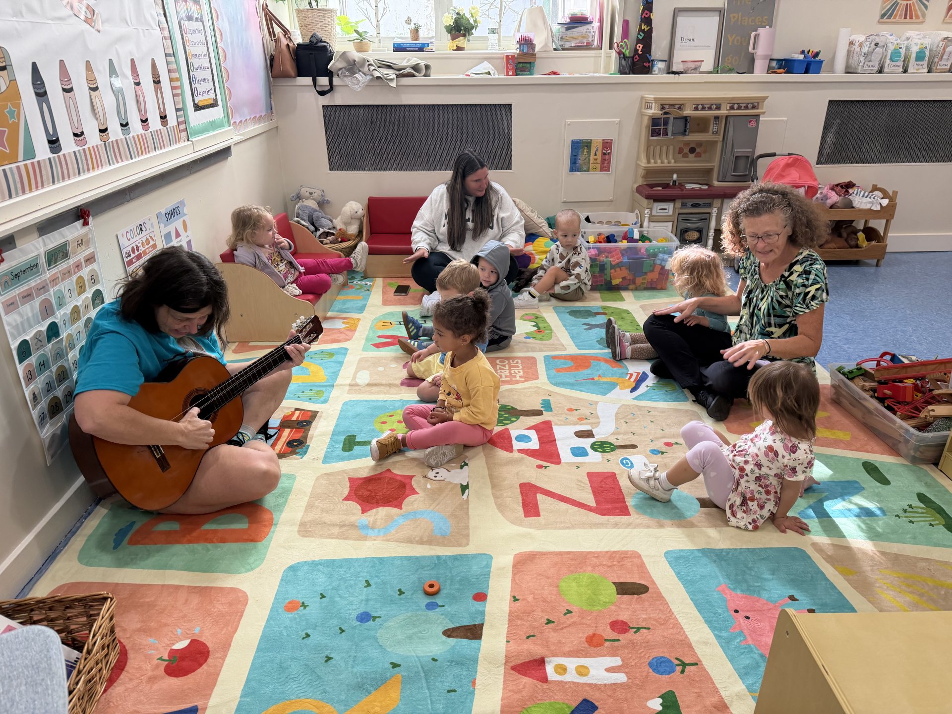 A teacher playing guitar for children sitting on the classroom rug